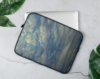 May include: Laptop sleeve featuring an abstract painting of a cloudy sky in shades of blue, yellow, and white. The sleeve has a black zipper and trim. The artwork is signed "Zugo" in the bottom right corner. The sleeve is on top of a silver laptop.