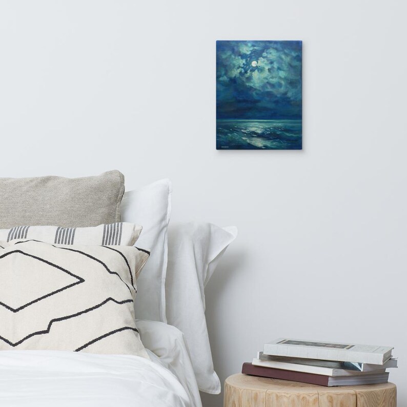 May include: A rectangular canvas art print depicts a moonlit seascape. The artwork features a full moon in a cloudy sky, with dark blue and teal hues dominating the scene. The ocean reflects the moonlight, creating a serene and atmospheric piece.