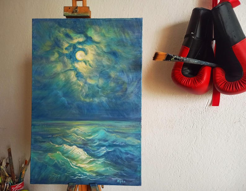 May include: An oil painting of a moonlit ocean scene in shades of blue and green, displayed on an easel. A pair of red and black boxing gloves hangs on the wall, with a paintbrush resting between them.