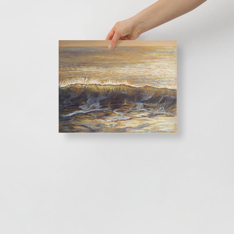 May include: A square print of an ocean wave, painted in shades of gold, brown, and blue. The wave crests with white foam, and the water reflects the sunlight. The artwork is held by a person.