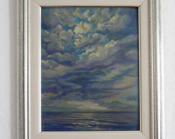 May include: An oil painting of a seascape with a dramatic sky. The artwork features a dark blue ocean under a sky filled with swirling clouds in shades of blue, gray, and yellow. The painting is framed in a silver-colored frame.
