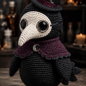 May include: A black and cream crocheted plague doctor doll wearing a top hat with a maroon band and a silver crescent moon charm. The doll features a long cream-colored beak mask, large black eyes, and a dark maroon cape with a silver moon clasp.