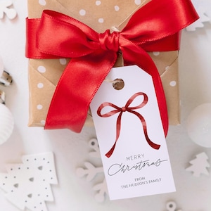 Puede incluir: Un regalo de Navidad envuelto en papel marrón con lunares blancos, atado con un lazo de satén rojo. Una etiqueta blanca con un diseño de lazo rojo dice "Feliz Navidad" y "De la familia Hudson".