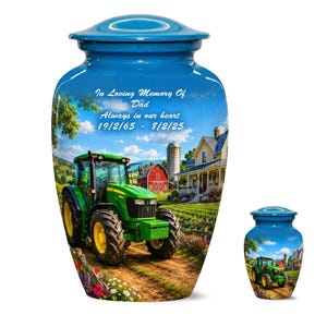 Op de afbeelding: Blauwe crematie-urn met een boerderijscène met een groene tractor, rode schuur en wit boerenhuis. De urn heeft een bijpassende kleinere aandenkenurn. Tekst luidt "In Loving Memory Of Dad" en data.