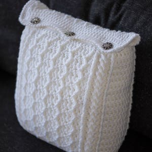 May include: White crocheted cushion with a diamond pattern and three decorative buttons. The cushion is on a dark grey surface.