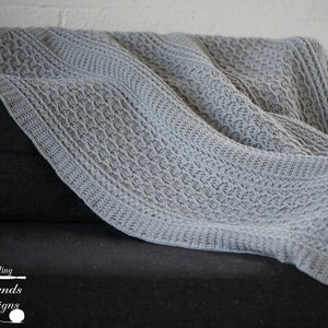 May include: A gray crocheted throw blanket with a cable knit pattern is draped over a black couch.