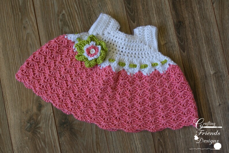 Peut inclure: Une robe de b&eacute;b&eacute; en crochet avec un corsage rose et blanc et une jupe rose. La robe est orn&eacute;e d'une fleur verte et blanche.