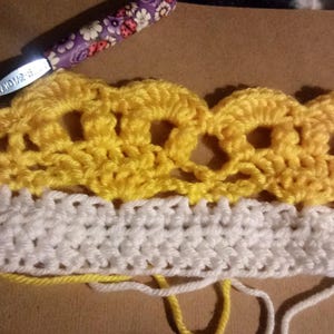 May include: Close-up of a crocheted piece with a yellow and white color scheme. The top portion is a yellow crocheted lace pattern, and the bottom portion is a white crocheted fabric.