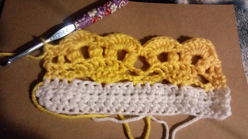 May include: Close-up of a crocheted piece with a yellow and white color scheme. The top portion is a yellow crocheted lace pattern, and the bottom portion is a white crocheted fabric.