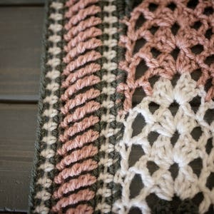 May include: Close-up of a crocheted blanket with a pink, white, and green color scheme. The blanket is made with a variety of stitches and patterns.