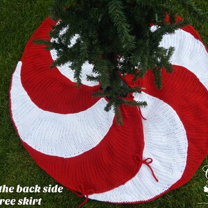 May include: Red and white crocheted Christmas tree skirt with a candy cane design. The skirt is shown from the back side, with the tree trunk in the center.