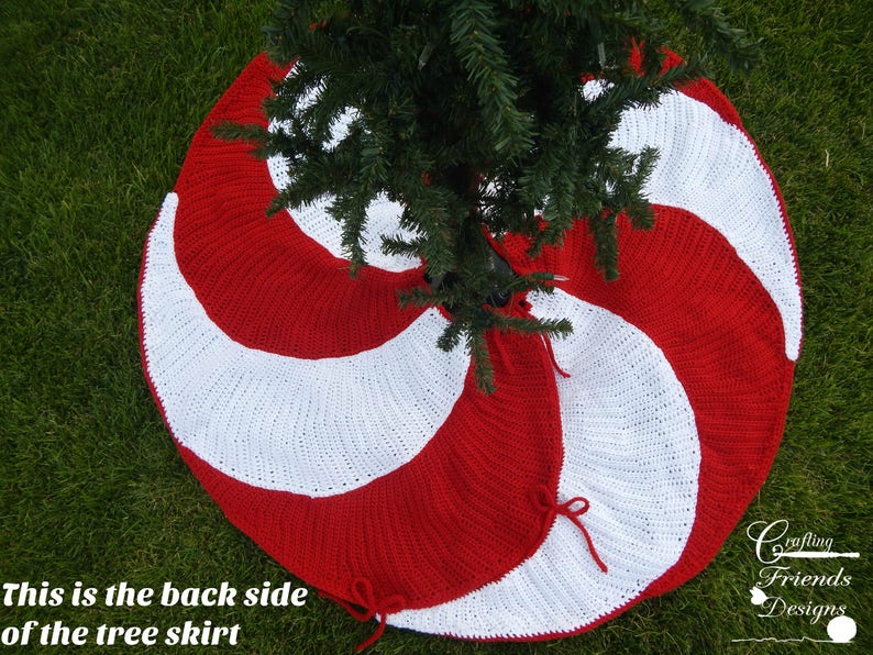 May include: Red and white crocheted Christmas tree skirt with a candy cane design. The skirt is shown from the back side, with the tree trunk in the center.