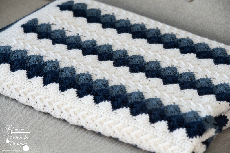 May include: A white and blue crocheted blanket with a chevron pattern. The blanket is made with a variety of shades of blue yarn, creating a gradient effect.