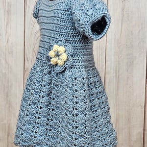May include: A light blue crocheted dress with a yellow flower embellishment. The dress has short sleeves and a flared skirt.