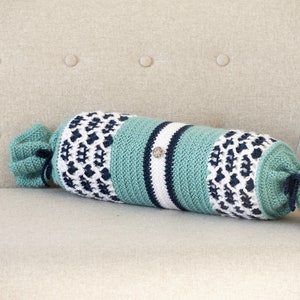 May include: A crocheted bolster pillow with a blue, white, and green striped pattern. The pillow is on a light beige couch.