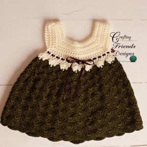 Peut inclure: Une robe de b&eacute;b&eacute; en crochet de couleur marron et blanche. La robe a un ourlet festonn&eacute; et un ruban marron nou&eacute; &agrave; la taille. La robe est r&eacute;alis&eacute;e avec un point textur&eacute; et a une d&eacute;licate bordure en dentelle autour de l'encolure.