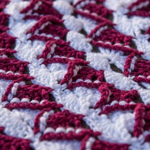 May include: Close-up of a crocheted fabric with a repeating pattern of burgundy and white triangles. The fabric is textured and has a soft, fuzzy appearance.
