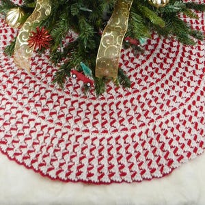May include: A red and white crocheted Christmas tree skirt with a scalloped edge. The skirt is made with a textured stitch pattern.