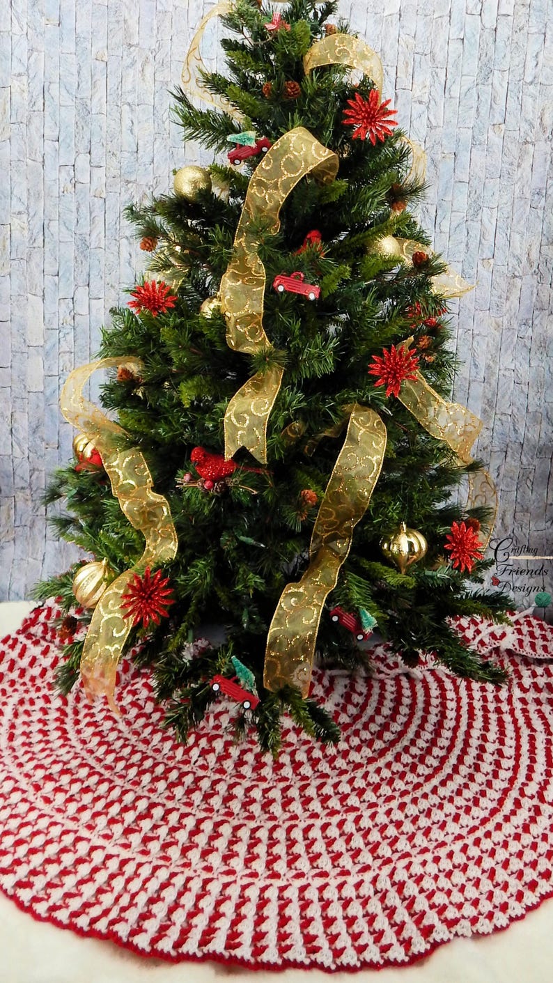 May include: A red and white crocheted Christmas tree skirt with a green Christmas tree decorated with gold ribbon and red ornaments in the background.