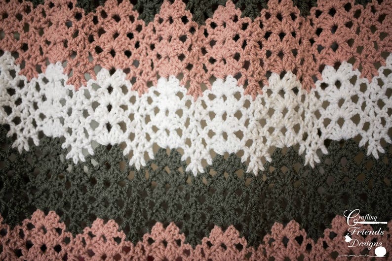 May include: A close-up of a crocheted blanket with alternating rows of pink, white, and green. The blanket has a lacy pattern and is made with a soft yarn.