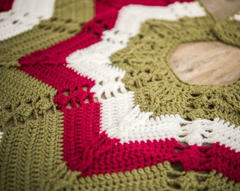 May include: A crocheted Christmas tree skirt in green, white, and red. The skirt is made of a thick yarn and has a scalloped edge.