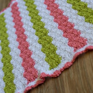 Peut inclure: Une couverture au crochet avec un motif en chevron rose, vert et blanc.