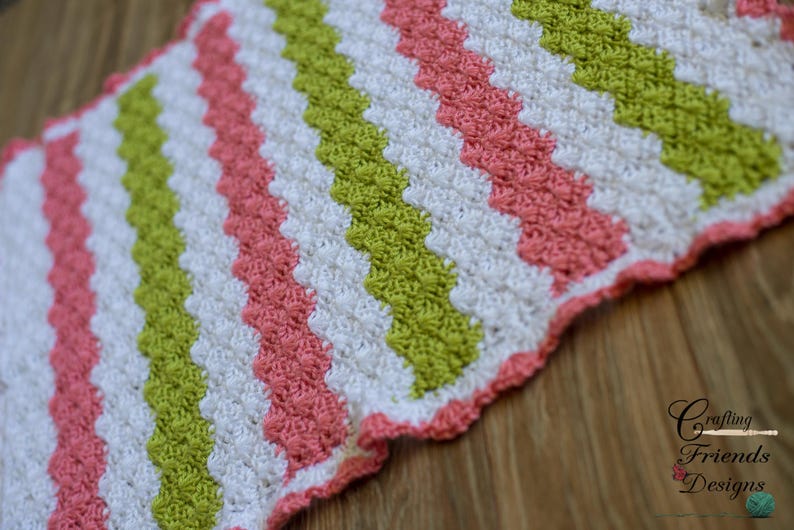 Peut inclure: Une couverture au crochet avec un motif en chevron rose, vert et blanc.