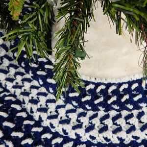 May include: A blue and white crocheted tree skirt with a geometric pattern. The skirt is made of soft yarn and has a fluffy texture.