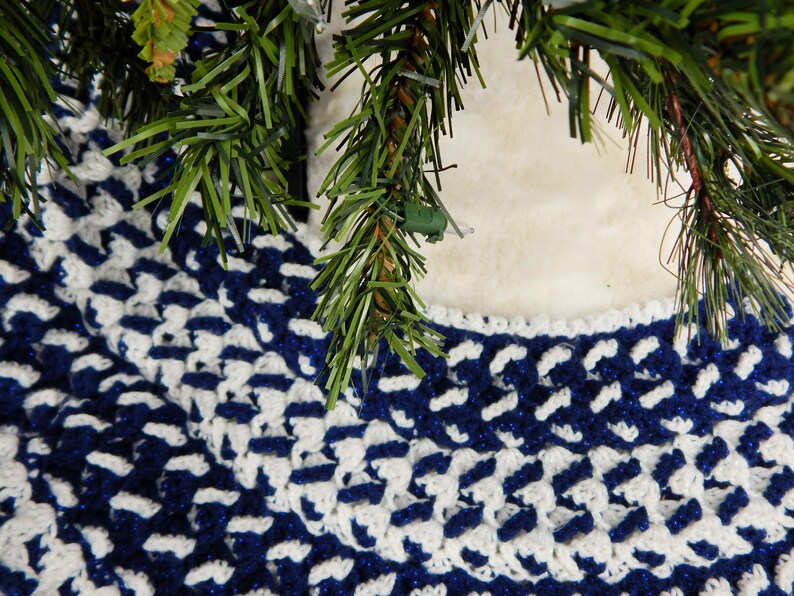 May include: A blue and white crocheted tree skirt with a geometric pattern. The skirt is made of soft yarn and has a fluffy texture.