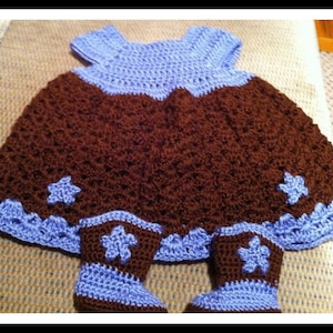 May include: A brown and blue crocheted baby dress with matching booties. The dress has a brown skirt with a blue bodice and a scalloped edge. The booties have a brown top with a blue cuff.