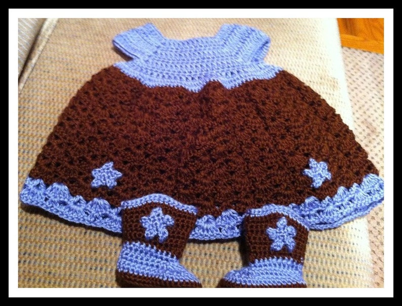 May include: A brown and blue crocheted baby dress with matching booties. The dress has a brown skirt with a blue bodice and a scalloped edge. The booties have a brown top with a blue cuff.