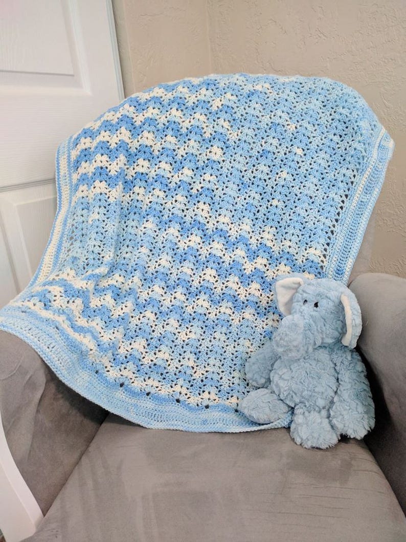 May include: A blue and white crocheted baby blanket with a blue plush elephant toy sitting on top of it.