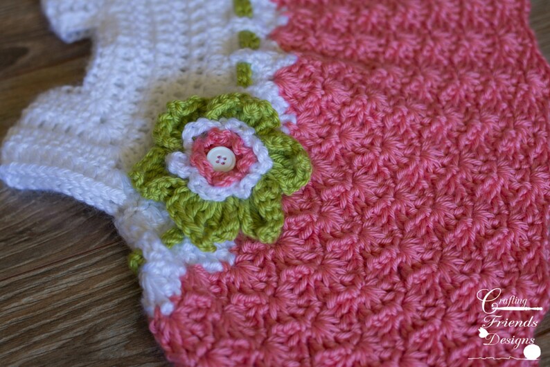 Peut inclure: Une robe de b&eacute;b&eacute; en crochet avec un corsage blanc et une jupe rose. La robe est orn&eacute;e d'une applique de fleur verte et blanche.