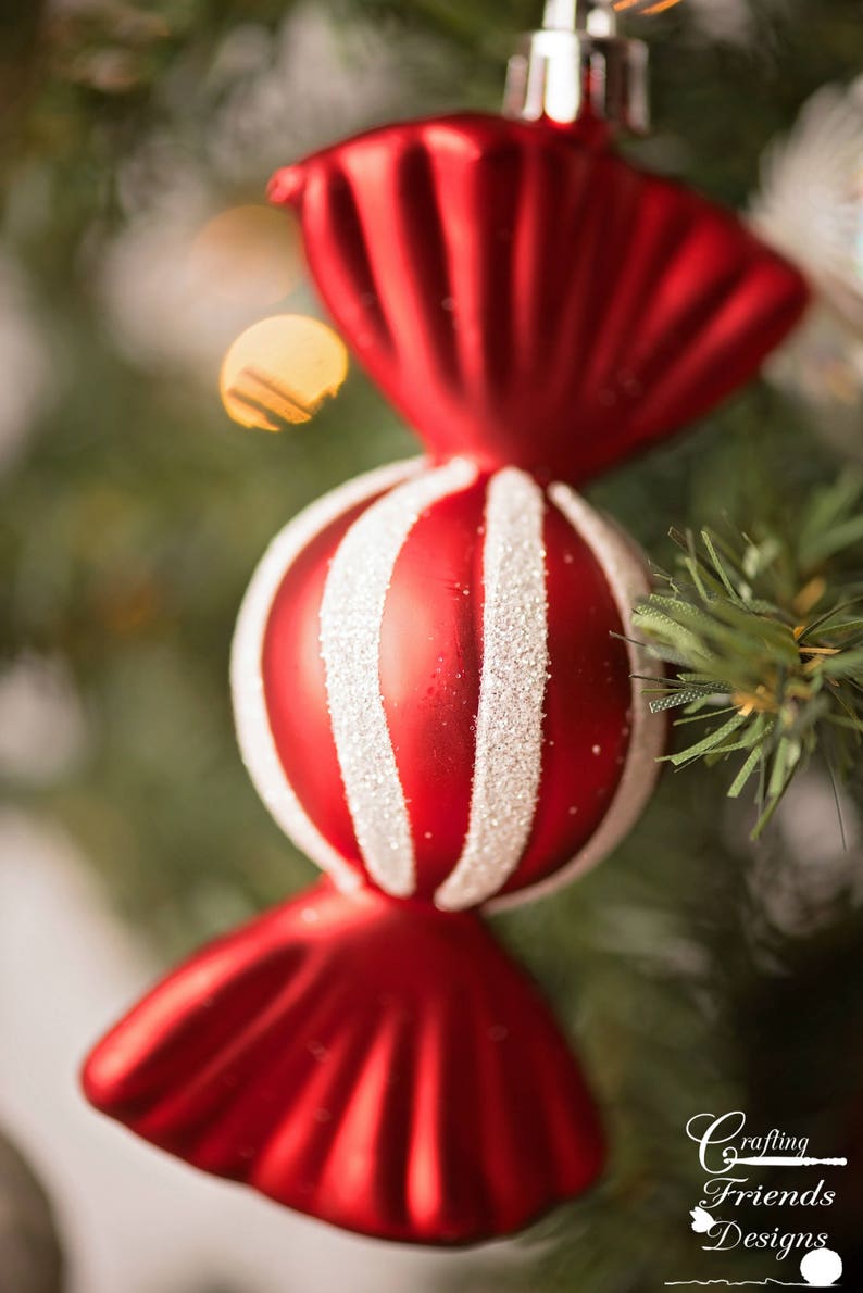 May include: Red and white candy cane Christmas ornament hanging on a green Christmas tree. The ornament is shaped like a candy cane with a red and white striped center and red ends.