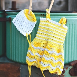 May include: A yellow and white crocheted baby dress and matching hat hanging on clothes pins. The dress has a striped pattern and the hat has a sun shape on the top.