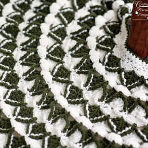 May include: Close-up of a crocheted doily with a white and green geometric pattern. The doily is made with a delicate stitch and has a scalloped edge.