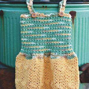 May include: A crocheted baby dress with a green and yellow striped bodice and a yellow crochet skirt. The dress is hanging on a clothesline with wooden clothespins.
