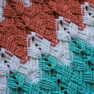 May include: Close-up of a crocheted blanket with a chevron pattern in coral, white, and teal colors. The blanket is made with a woven stitch and has a textured look.