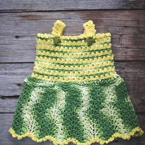 May include: A crocheted baby dress with yellow and green stripes. The dress has a scalloped hem and is decorated with small green leaves.