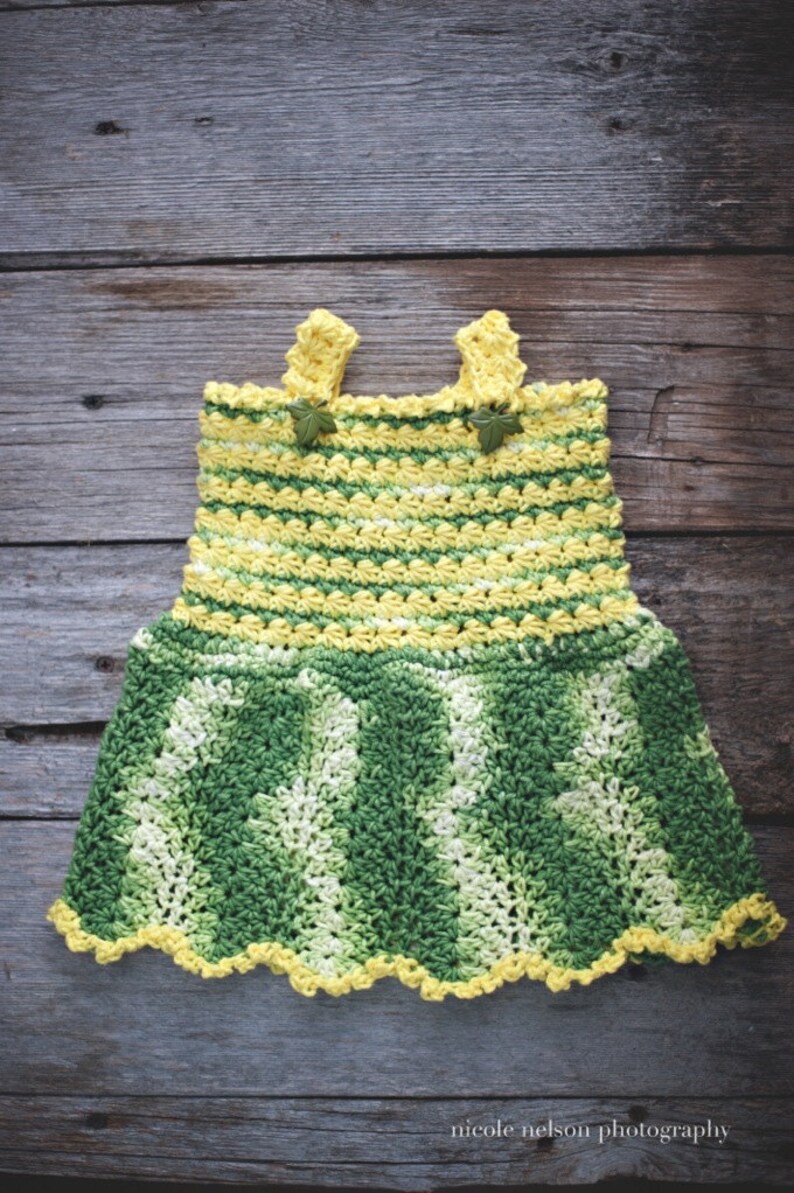 May include: A crocheted baby dress with yellow and green stripes. The dress has a scalloped hem and is decorated with small green leaves.
