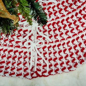 May include: Red and white crocheted Christmas tree skirt with white bows. The skirt is made with a textured stitch pattern.