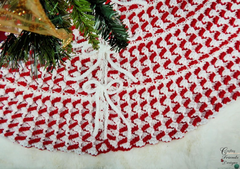 May include: Red and white crocheted Christmas tree skirt with white bows. The skirt is made with a textured stitch pattern.