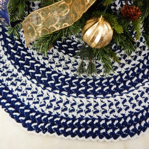 May include: A crocheted Christmas tree skirt in a navy blue and white chevron pattern. The skirt is made with a thick yarn and has a scalloped edge.