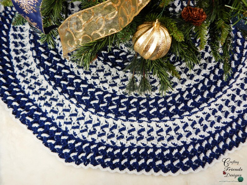 May include: A crocheted Christmas tree skirt in a navy blue and white chevron pattern. The skirt is made with a thick yarn and has a scalloped edge.