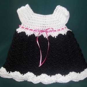 Peut inclure: Une robe de b&eacute;b&eacute; en crochet noir avec une bordure en crochet blanc et un ruban rose.