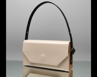 May include: Cream-coloured rectangular handbag with a black handle. The bag has a flap closure and wooden side panels. The handle is attached to the bag with black hardware. The bag is reflected in the shiny surface below.