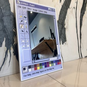 Può includere: Uno specchio rettangolare incorniciato per assomigliare all'interfaccia classica dell'applicazione Windows Paint. Lo specchio presenta un bordo azzurro con la barra del titolo "untitled - Paint" e una barra degli strumenti con icone. Il riflesso mostra una stanza con una scrivania in legno.