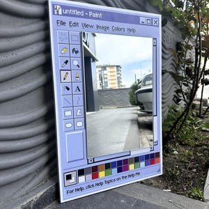 Può includere: Uno specchio rettangolare incorniciato per assomigliare alla classica interfaccia dell'applicazione Windows Paint. La cornice azzurra presenta la barra del titolo, le opzioni del menu e una tavolozza di colori. Il testo "untitled - Paint" è visibile. Lo specchio riflette una scena all'aperto.