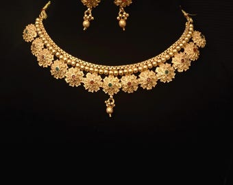 May include: A gold-colored necklace and earring set. The necklace features a floral design with red and green accents. The matching earrings have a similar floral design. The jewelry is displayed against a black background.