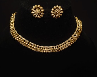 May include: A gold-colored jewelry set featuring a necklace and matching earrings. The necklace has a beaded design, and the earrings are flower-shaped studs. The set is displayed on a black background.